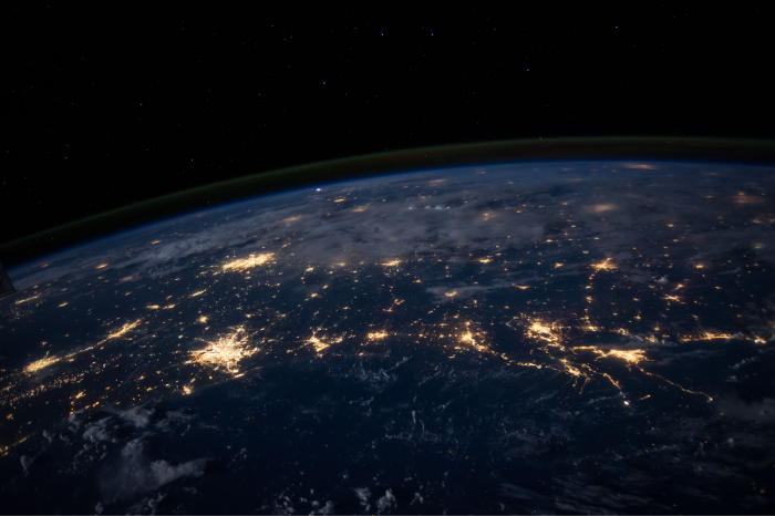 View of Earth from space at night showing illuminated city lights and dark sky filled with stars.